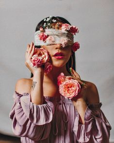 a woman with flowers in her hair holding roses up to her face and covering her eyes