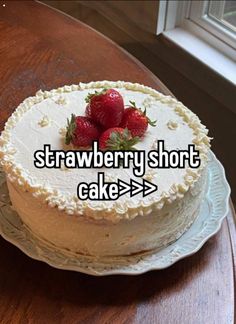 a white cake with strawberries on top sitting on a table next to a window