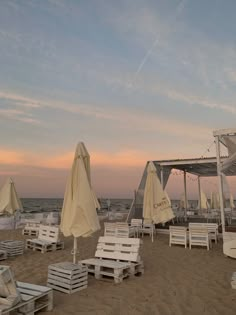 white chairs and umbrellas on the beach at sunset