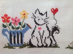 a cross - stitch picture of a cat and flower pot with hearts on it's side