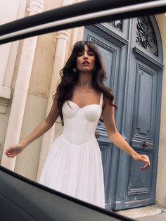 a woman standing in front of a blue door wearing a white dress and holding her arms out