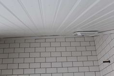 a bathroom with white tile walls and a ceiling mounted air conditioner in the corner