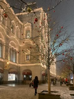 people are walking around in front of a building with christmas lights on the windows and trees