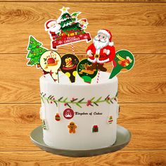 a cake decorated with christmas stickers on top of a wooden table next to a wood wall