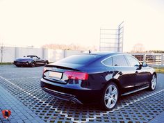 a black car parked in a parking lot next to other cars on the pavement and fenced area