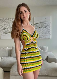 a woman in a yellow and green dress standing next to a white couch with her hands on her hips