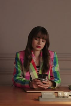 a woman sitting at a desk holding a cell phone and looking down with her eyes closed