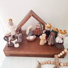 small crocheted nativity figurines are displayed on a wooden shelf with beads