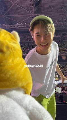 a young boy standing next to a yellow teddy bear at a sporting event in front of an audience