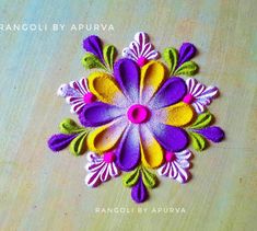 an image of a colorful flower made out of felt on a wooden table with text overlay that reads rangoli by apurva