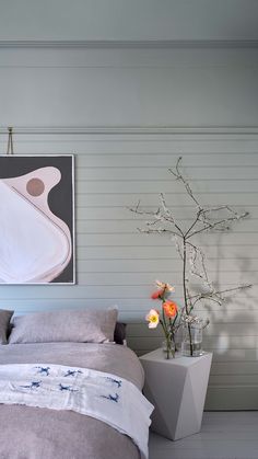 a bedroom with a large painting on the wall next to a bed and flowers in a vase