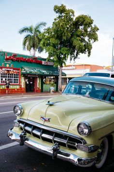 an old car is parked on the side of the road in front of a store