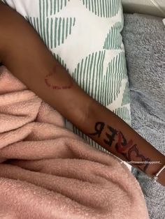 a woman with a tattoo on her arm laying in bed next to a pink blanket