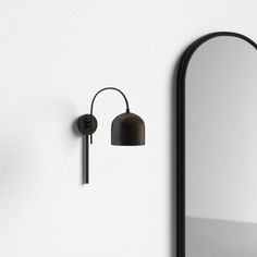 a black wall mounted light next to a mirror and lamp shade on a white wall