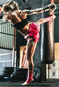 a woman kicking a punching bag with her leg in the air while wearing red shorts