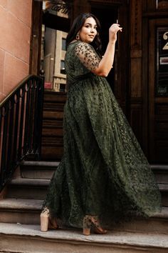 a woman in a long green dress is standing on the steps and holding an umbrella