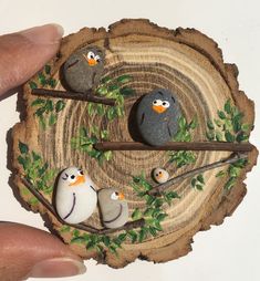 a hand holding a piece of wood with birds painted on it and three small rocks in the middle