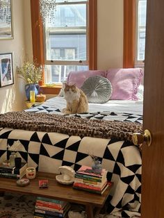 a cat sitting on top of a bed next to a table with books and cups