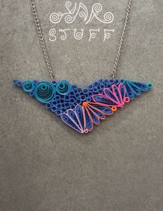 a necklace made out of paper and string with an intricate design on the front, sitting on a gray surface