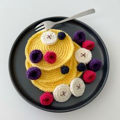 a crocheted cake on a plate next to a fork and knife with buttons