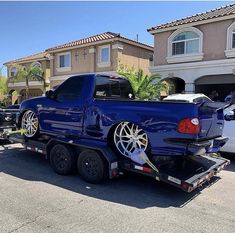 a blue truck parked in front of a house with its flatbed trailer attached to it