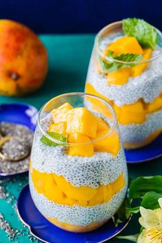 two glasses filled with fruit on top of a blue plate next to an orange and white flower