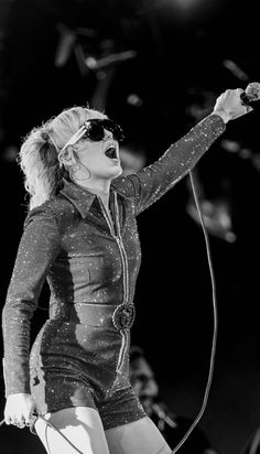 a woman singing into a microphone while holding her hands out to the side with one hand