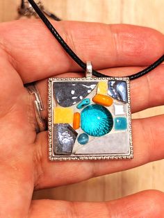 a hand holding a square pendant with an image of a bird on it's side