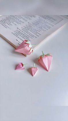 three pink origami hearts are on top of an open book, next to the pages