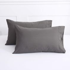 two gray pillows sitting on top of a white bed