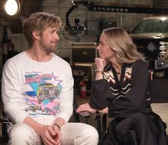 a man and woman sitting next to each other in front of a camera on a chair