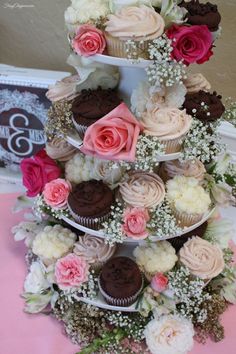 three tiered cupcake display with pink and white flowers on the top, chocolate cupcakes in the middle