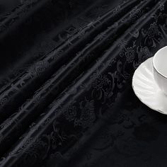 a white cup and saucer sitting on top of a black cloth covered tablecloth