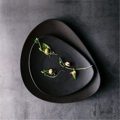 a black plate topped with flowers on top of a gray table next to a knife and fork