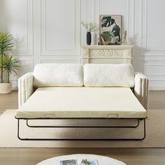 a white couch sitting on top of a wooden floor next to a table with a potted plant