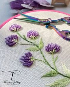 a close up of some scissors and purple flowers on a white cloth with pink trim