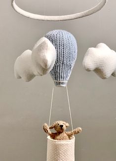 a stuffed animal in a knitted basket suspended from a string with two balls attached to it