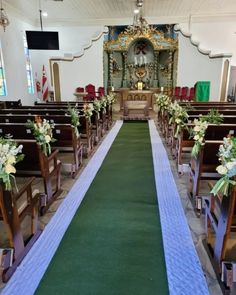 an empty church with rows of pews and flower arrangements on the aisle, along with green carpeting