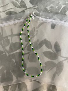 a green and white beaded necklace sitting on top of a sheered cloth covered bag