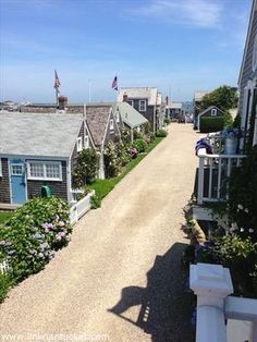 a gravel road leading to several small houses on the ocean side with flags flying in the wind