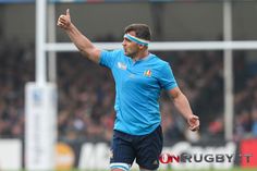 a man in blue shirt and shorts on field with his hand up to the sky