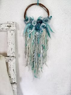 a wall hanging on the side of a white building with blue flowers and feathers attached to it