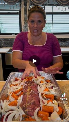 a woman standing in front of a pan filled with meat and vegtables