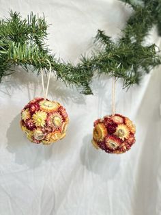 two ornaments hanging from a tree branch on white fabric with pine branches in the background