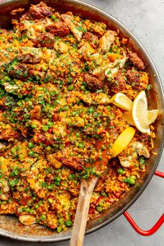 a pan filled with rice, peas and meat next to a wooden spoon on top of a table