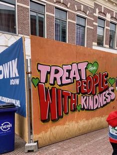 a woman walking down the street in front of a wall that says treat people with kindness