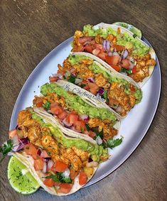 three tacos on a plate with guacamole and tomatoes