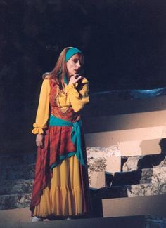 a woman in a colorful dress standing on stage with her hands clasped to her chest