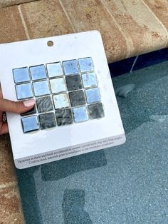 a person is holding up a white and blue mosaic tile