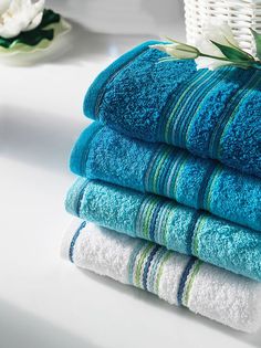 four towels stacked on top of each other in front of a basket and flower arrangement